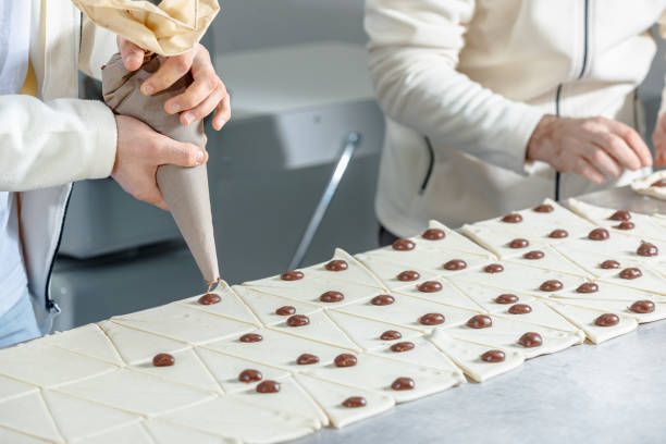 istock Pastry chefs working on the kitchen counter, squeezing chocolate cream drops on dough and making crescent rolls 1807489114