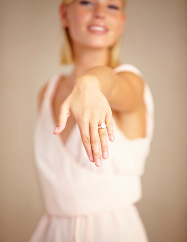 A beautiful young woman with arm outstretched displaying a engagement ring on her hand with selective focus