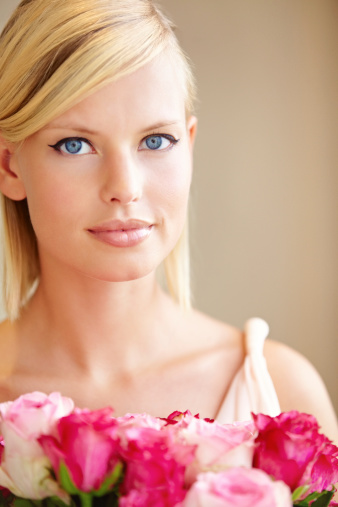 Portrait of a beautiful young woman holding a bouquet of pink roses and smiling