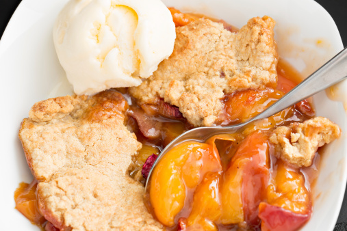 An overhead close up of a peach and rhubarb cobbler with a scoop of vanilla ice cream in a white bowl.