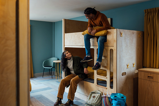 A wide shot of a man and woman wearing warm, casual clothing in a luxury hostel in the seaside town of Amble, Northumberland. They have checked into a dormitory room with bunkbeds. They sit on their beds and talk.