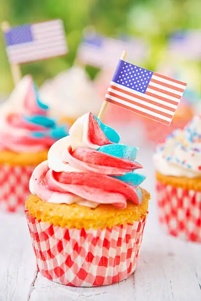 Red-white-and-blue cupcakes with American flags on an outdoor table.