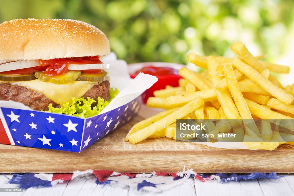 Hamburguesa con papas fritas sobre una mesa al aire libre en la luz brillante - Foto de stock de Aire libre libre de derechos