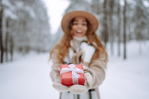 Beautiful woman in a winter forest holds a red gift in her hands. Holiday concept, relaxation.