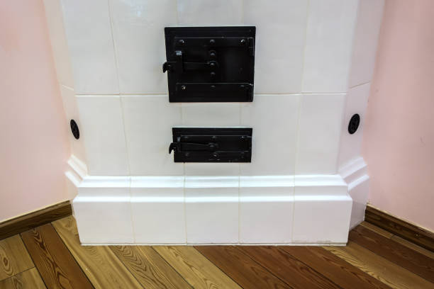 Close up an old fireplace restored in a modern interior. Restored antique oven with a ceiling height, lined with white tiles. Metal doors with latches are slightly covered with rust. Heating  appliances concept.