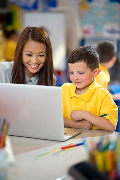 istock schoolboy with laptop and teacher 180753647
