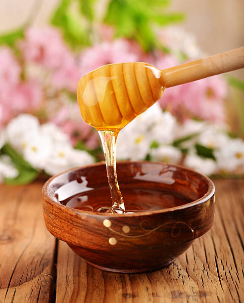 Honey dripping in to a wooden bowl stock photo