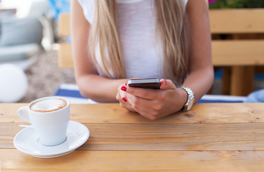Woman having a coffee and using her smartphone, texting message