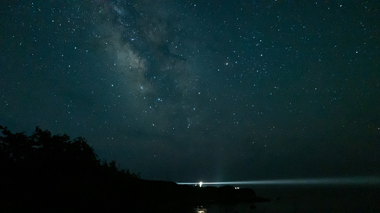 A ray of light from the lighthouse illuminates the stars of the Milky Way
