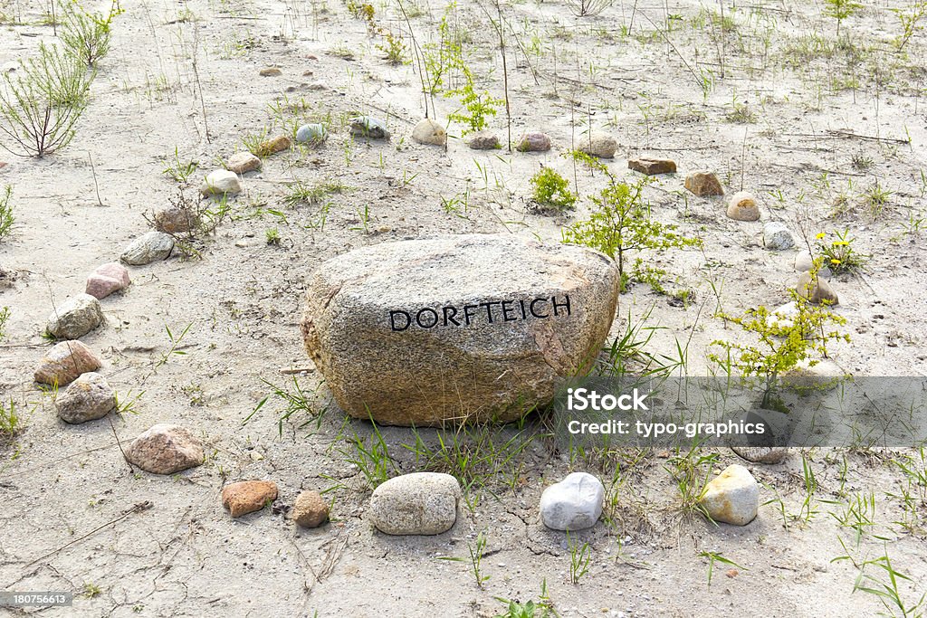 Symbol for a former village pond "Symbol for a former village pond. The word on the stone DORFTEICH means village pond. The village Wolkenberg near Welzow, Brandenburg, was destroyed for lignite mining (opencast mine Welzow-Sued). The village was completely excavated. The stones are remembering the place of the former village pond.For more pictures, please look here:" Boulder - Rock Stock Photo