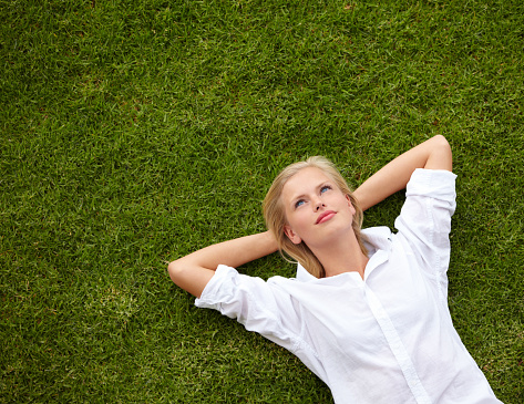 High angle shot of an attractive young woman relaxing on a grassy field and looking up at the sky