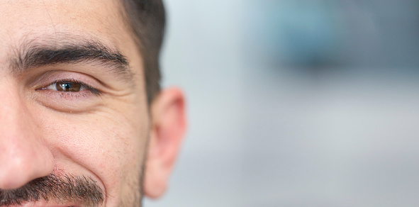 Face, eye and mockup with a man closeup for future vision or eyesight while looking happy or positive. Portrait, half and space with a handsome young male person posing on a blurred gray background