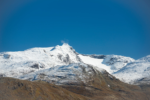 Hiking trail passes frozen lake and patches of snow in autumn colored high mountains after first snowfall of the season in Jotunheimen National Park in Norway. The snow of last season is still melting in some parts of the mountains. The image was captured with a full frame DSLR camera and a sharp fast lens.