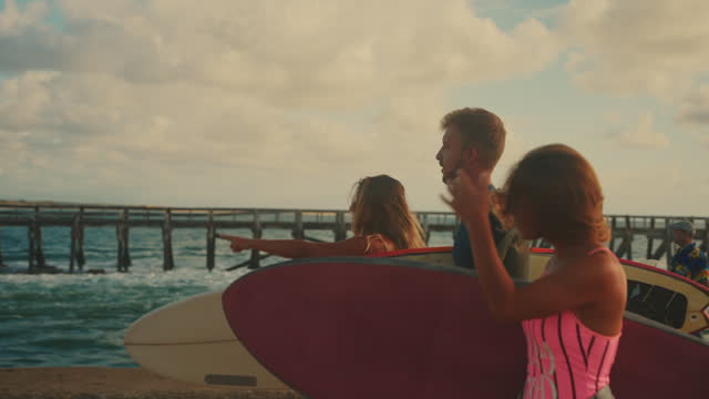 Surfer friends walking with surfboards along ocean pier. Enjoying summer