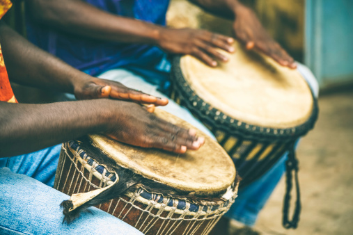 Two West African men playing djembe.