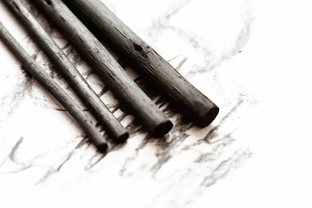 A group of fat and thin sticks of artist's charcoal make a few tentative scribbles on a sketchpad.