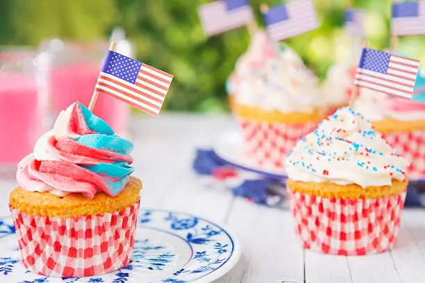 Red-white-and-blue cupcakes with American flags on an outdoor table.