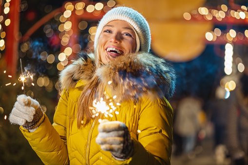 Young woman in yellow jacket holding sparklers and smiling. Christmastime in the city
