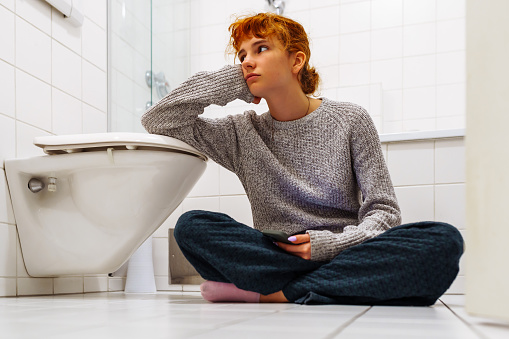 portrait teenage girl sitting in toilet on floor with phone in hand