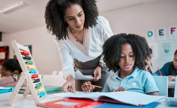 istock Math, education or teacher helping a child in a classroom with learning development, growth or studying. Writing, notebook or black woman teaching, talking or speaking to a young African boy student 1807675001