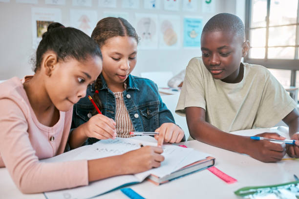 Teamwork, education and children with class project, working together in Montessori school at desk. Books, help and diversity, young students writing or drawing in notebook for math test or homework.