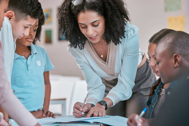 istock African teacher teaching children, helping students in classroom with homework and writing in book. Diversity in education, educator reading kids notebook and group learning together for assessment 1807677293