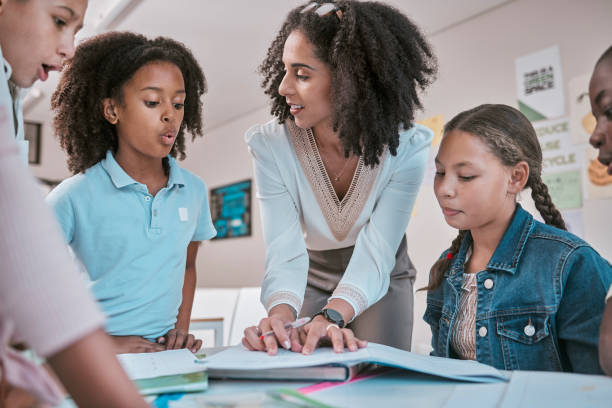 istock Female teacher asking student a question, children learning in classroom and sign homework in book. School for teaching, educator reading kids notebook and group working together for assessment 1807678365