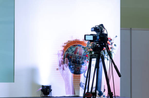 istock Back view video camera on tripod look to stage at business presentation exhibition 1807688500