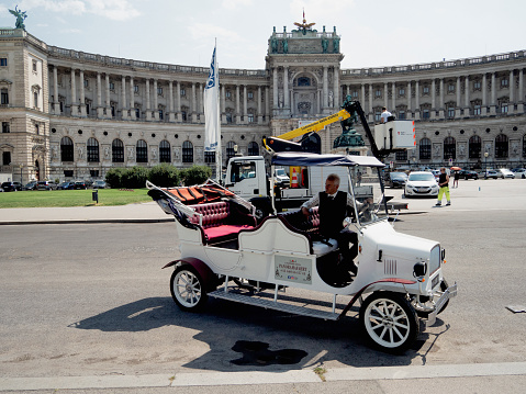 Vienna, Austria - August 16, 2023: A tuk-tuk driver waits for clients at the Heldenplatz square in Vienna.