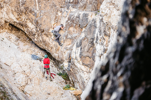 Young man climbing a steep mountain, using climbing equipment. His female friend helping him.