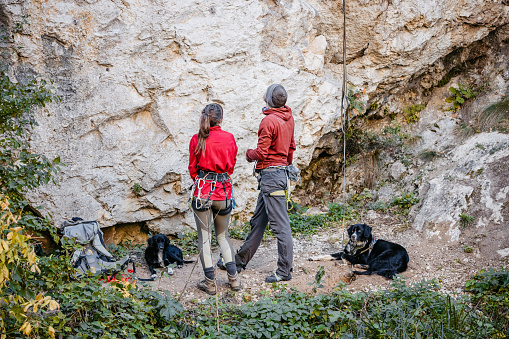 Young man and woman preparing to climb a steep mountain, using climbing equipment.