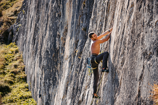 Young man climbing a steep mountain, using climbing equipment.