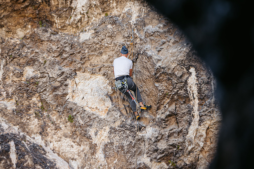 Mature man climbing a steep mountain, using climbing equipment.