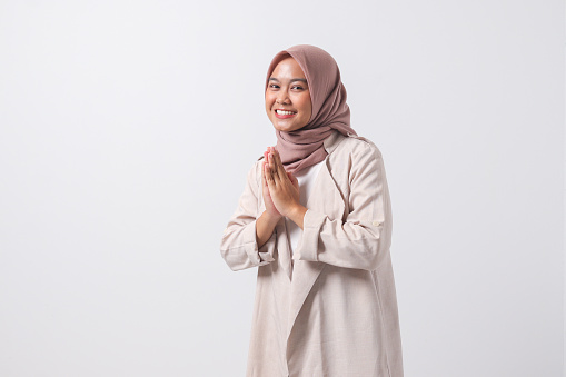 Portrait of excited Asian hijab woman in casual suit showing apologize and welcome hand gesture. Businesswoman concept. Isolated image on white background