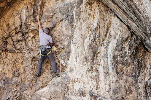 Young man climbing a steep mountain, using climbing equipment.