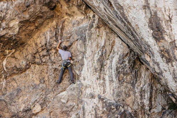 A young man is bouldering on Mt. Roothnaan with Chimney Rock behind him.