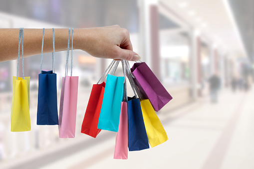 Crop female hand holding colorful paper bags on background of shopping center