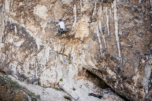 Mature man climbing a steep mountain, using climbing equipment.