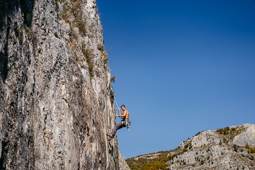 Young man climbing a steep mountain, using climbing equipment.
