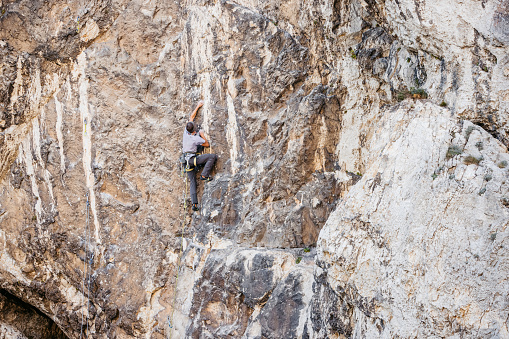 Young man climbing a steep mountain, using climbing equipment.