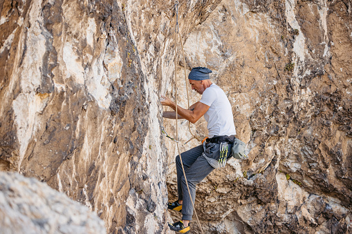 Mature man climbing a steep mountain, using climbing equipment.