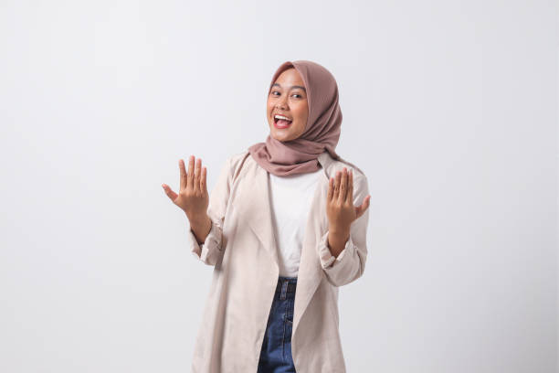 Portrait of excited Asian hijab woman in casual suit spreading her hands sideways. Greeting and welcoming someone. Inviting people to come in. Businesswoman concept. Isolated image on white background stock photo