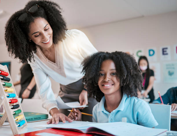 istock Young child learning maths, happy teacher in classroom with children and knowledge at desk. Female educator writing in workbook, reading kids notebook at school and teaching student with assignment 1807747402