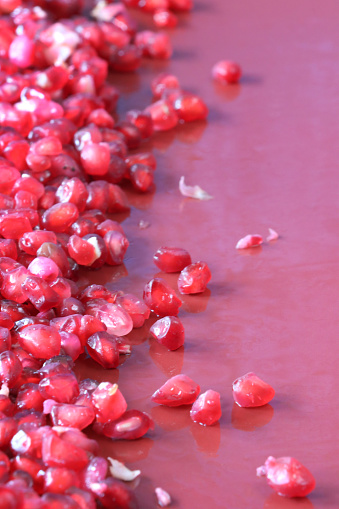 Stock photo showing a close-up, elevated view of healthy eating image of a pile of pomegranates (Punica granatum) seeds displaying red flesh (arils) encasing seeds on a red background.