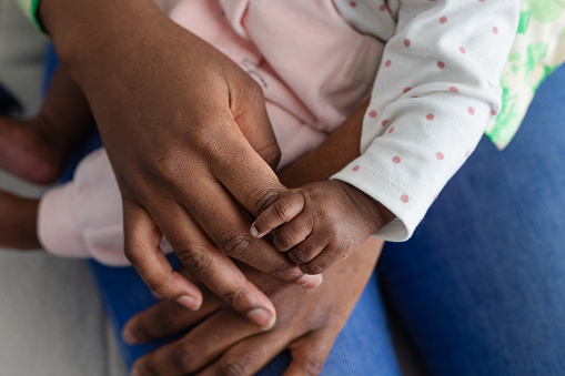 Close up off a mother holding her newborn baby's hand while sitting on a sofa bonding with her. They are at their home in Sedgefield, North East England.