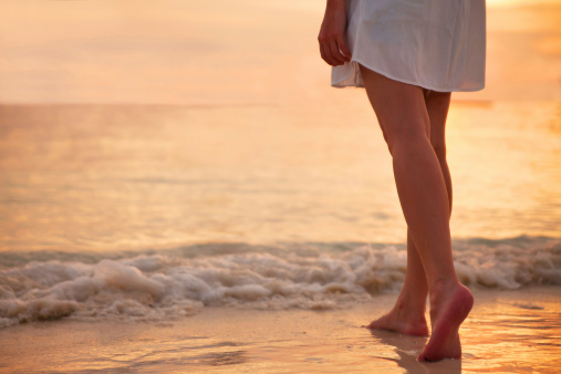 Young woman in white dress walking alone on the beach in the sunset