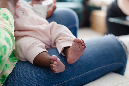 Mother holding her newborn baby on a sofa bonding with her. They are at their home in Sedgefield, North East England. Focus is on the baby's feet.