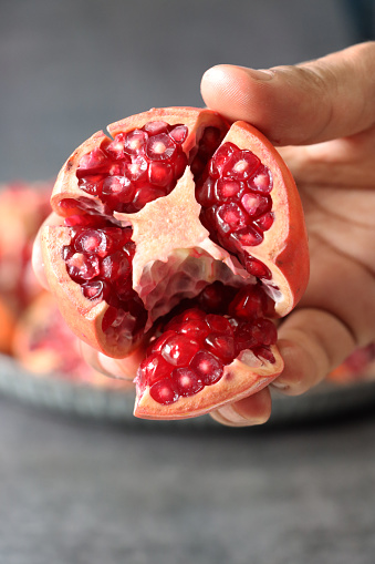 Stock photo showing close-up view of healthy eating image of an unrecognisable person holding
opened pomegranate (Punica granatum), displaying red-pink peel (epicarp), white mesocarp (albedo) and red flesh (arils) encasing seeds.