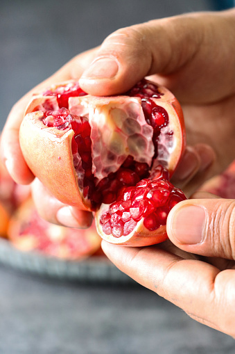 Stock photo showing close-up view of healthy eating image of an unrecognisable person holding\nopened pomegranate (Punica granatum), displaying red-pink peel (epicarp), white mesocarp (albedo) and red flesh (arils) encasing seeds.