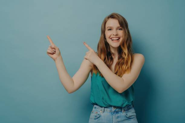 istock Joyful young woman pointing upwards with both hands, delighted expression on a teal background 1807799063